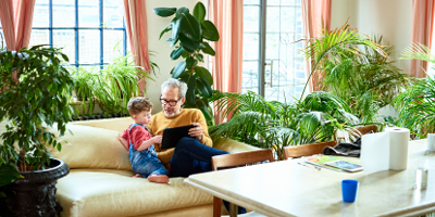 Grandfather and grandson on couch surrounded by indoor plants looking at a tablet screen.