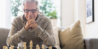 Older gentleman sitting on his couch, contemplating his next move in chess