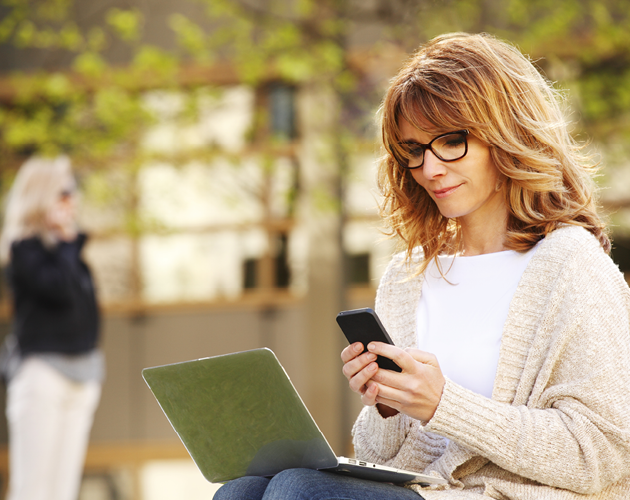 Woman using phone and laptop outside