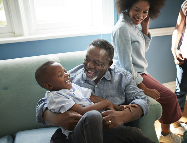 Father tickling son on couch with daughter looking on