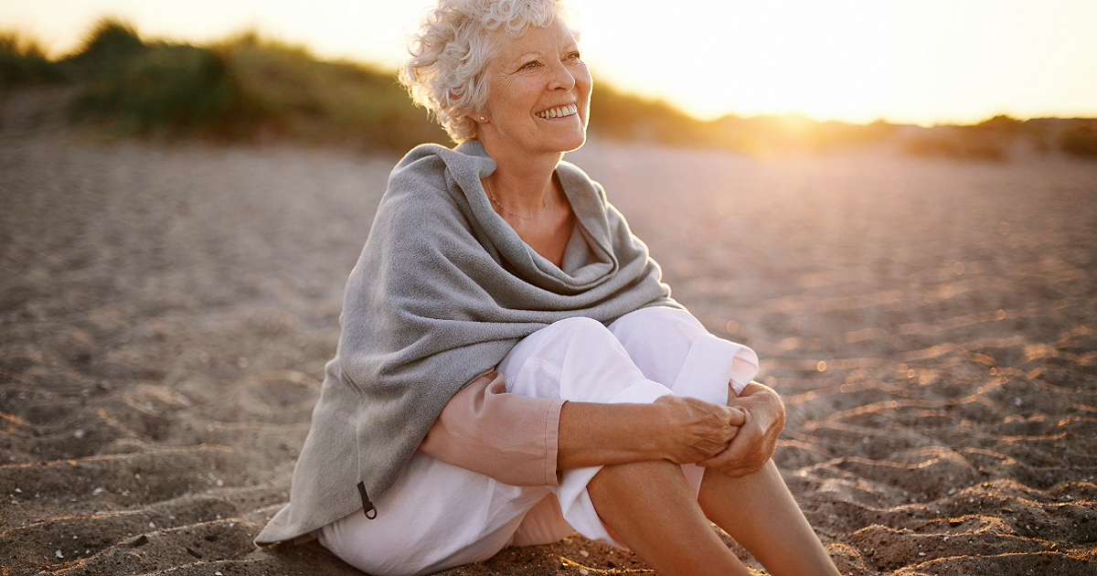 Smiling senior woman sitting on a beach.
