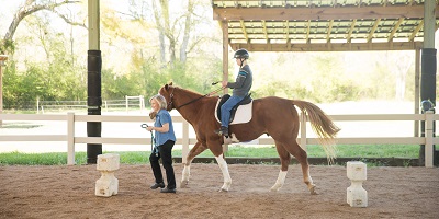 Child riding horse guided by Special Equestrians volunteer